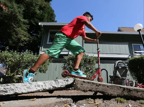 A youngster rides his scooter over a sidewalk buckled by an earthquake Sunday, Aug. 24, 2014, in Napa, Calif.  
